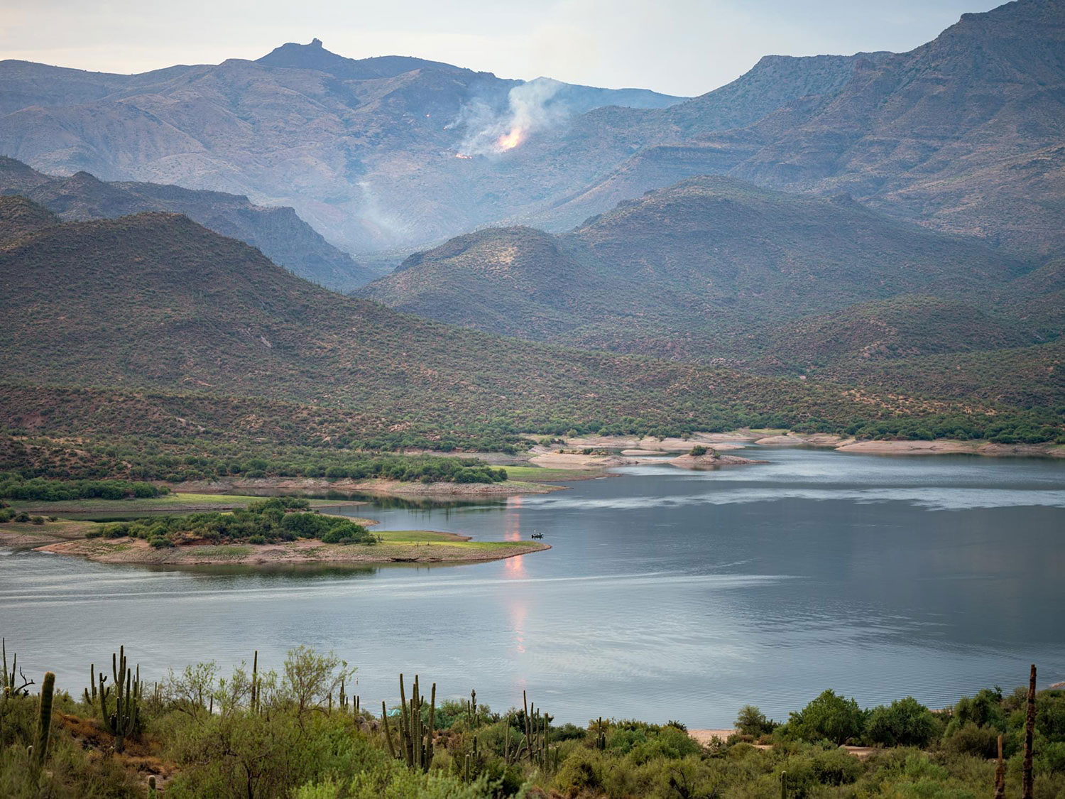 An early-morning angler fishes on Bartlett Lake, northeast of Phoenix, as a wildfire burns nearby. By Kurt Kamka