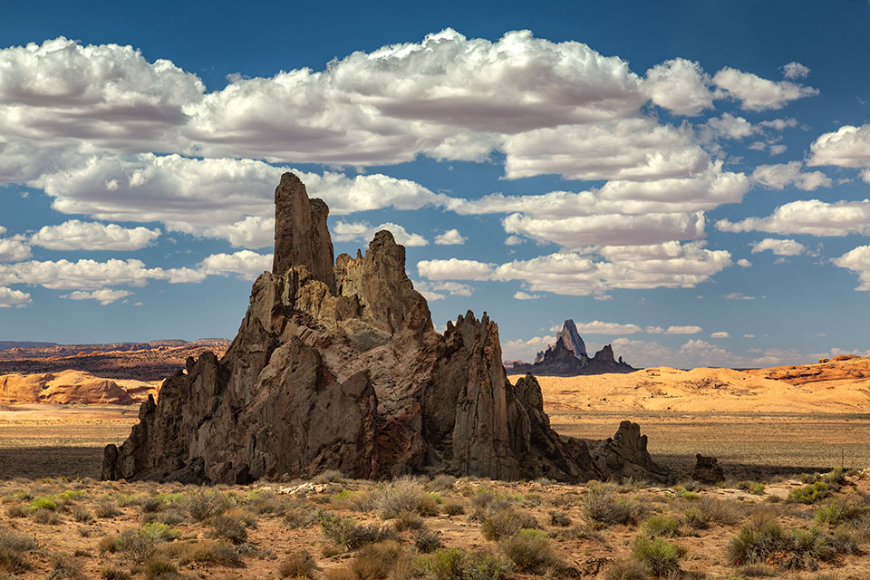 Scattered clouds shade Church Rock, near Kayenta on the Navajo Nation, as Agathla Peak looms to the north. Both landmarks are eroded volcanic plugs and are part of the Navajo Volcanic Field, which formed about 25 million years ago. By Larry Lindahl