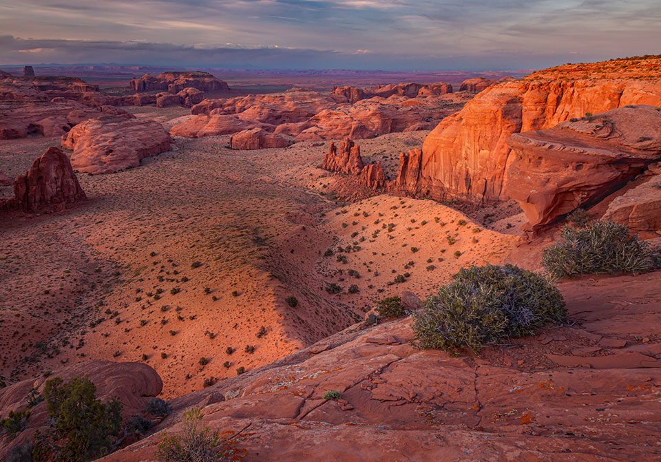 Shadows cloak the sandstone buttes of Monument Valley in a sunset view from Hunts Mesa, which forms the valley’s southeastern edge. Monument Valley is one of the high-desert landscapes that make up much of the Colorado Plateau. By Larry Lindahl