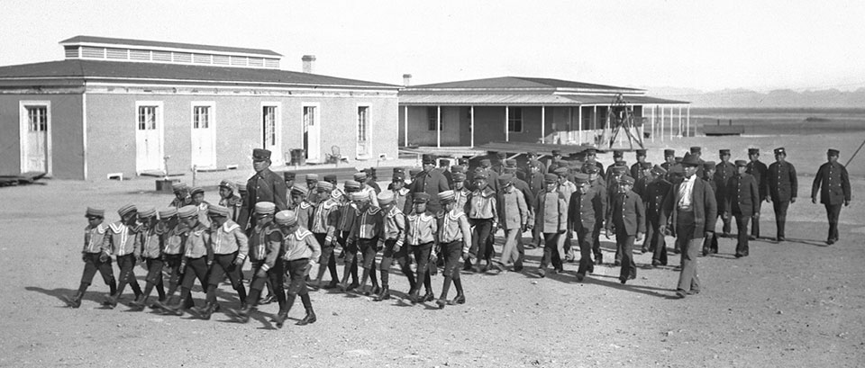 Students likely from the Fort Yuma-Quechan Tribe march in front of a boarding school in the Yuma area around 1900. | University of Southern California Digital Library, California Historical Society Collection