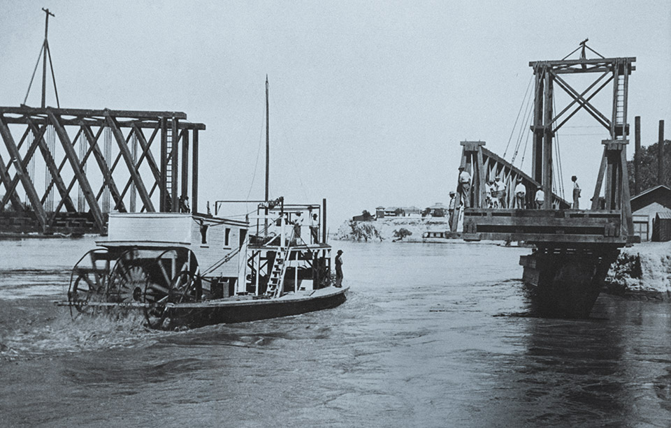 The gas-powered riverboat Aztec passes through a movable bridge at Yuma in 1902. The Aztec moved cargo on the Colorado River between Yuma and Needles, California, until 1905, when a severe sandstorm caused it to wreck a few miles downstream from Needles. | THE HUNTINGTON LIBRARY