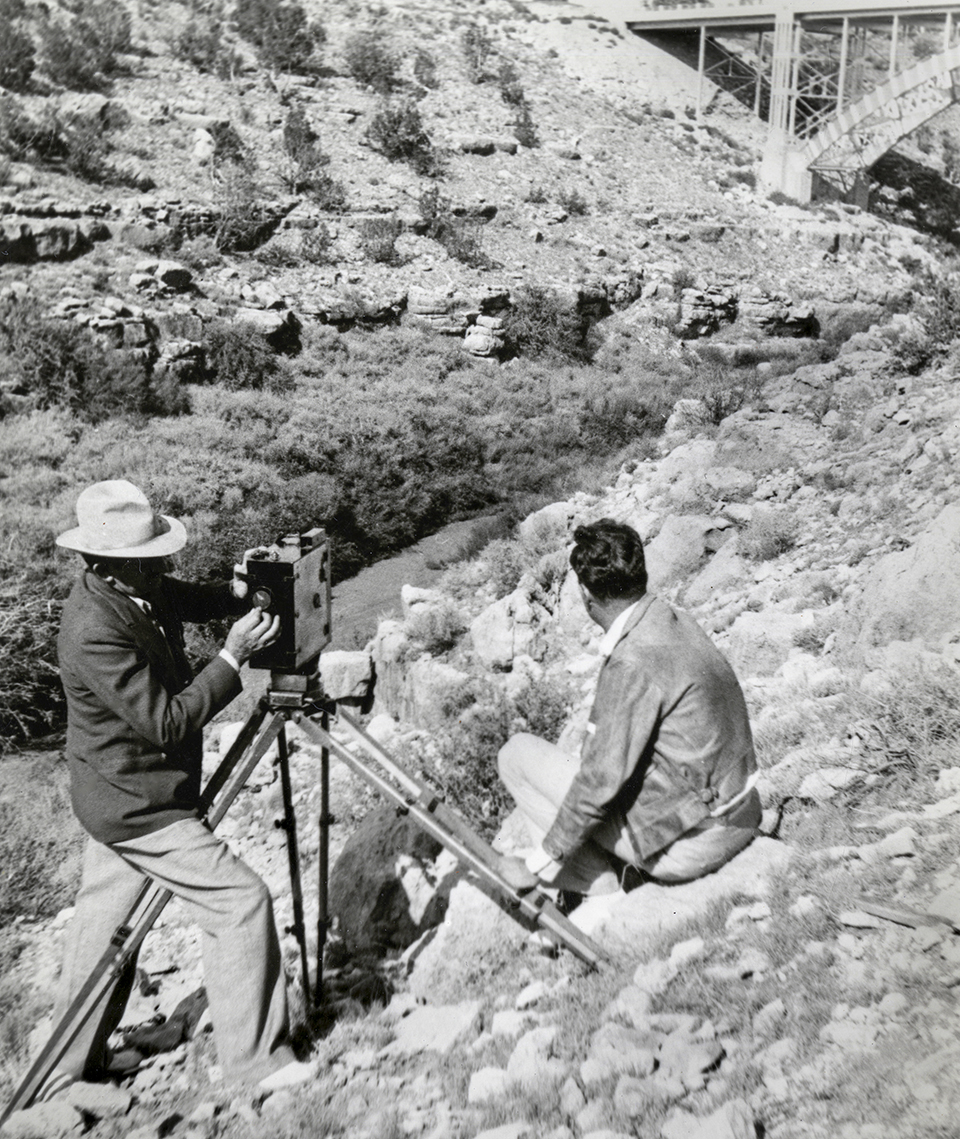 Wallace (left) and an unidentified assistant position a camera on a rocky slope to photograph a highway bridge. | Arizona Historical Society