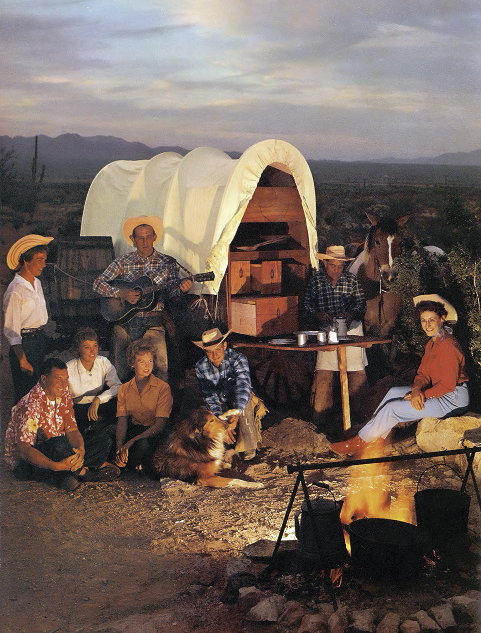 A chuckwagon campfire is enjoyed by several men and women dressed in western gear. By Ray Manley