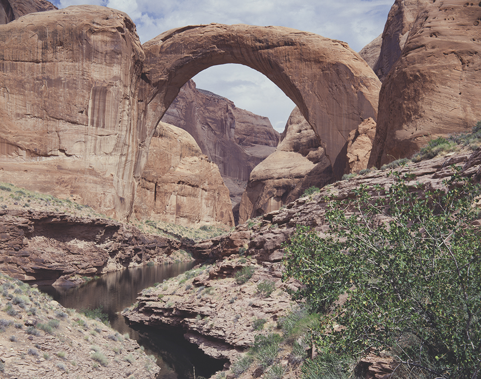 Rainbow Bridge arches over a sandstone landscape on the north side of Lake Powell. Despite often being described as an Arizona attraction, Rainbow Bridge is about 5 miles north of the state line, in Utah. By Josef Muench