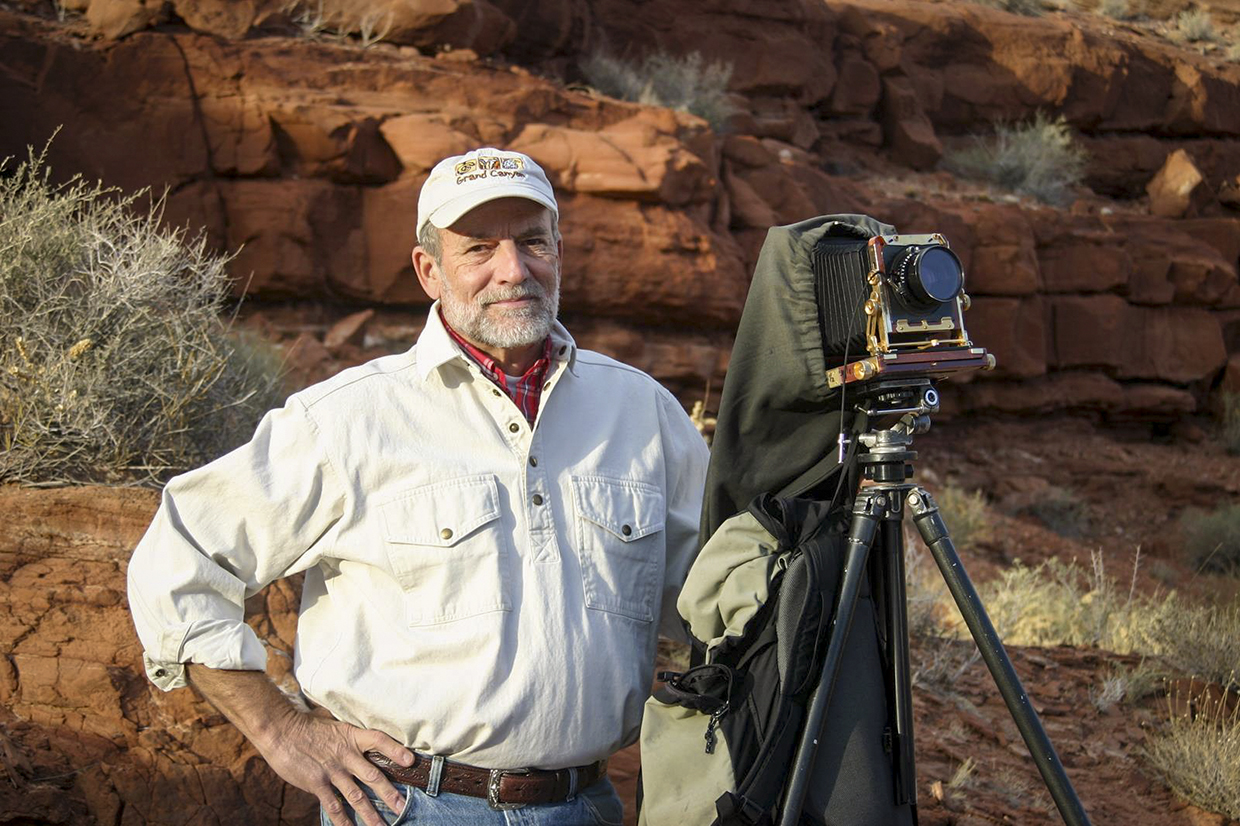 Portrait of Gary Ladd with 4x5 camera against a backdrop of red rocks is by Renee Roundtree.