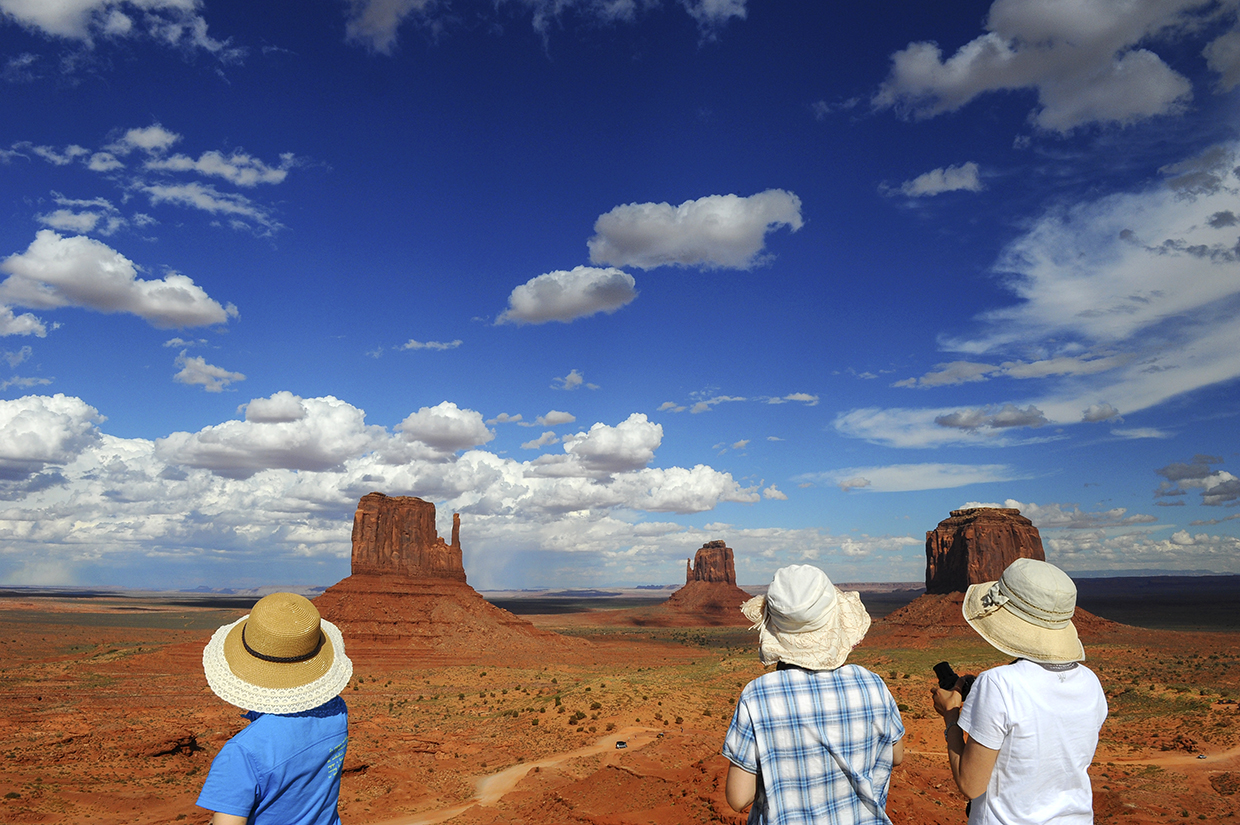 Three Japanese tourists take in a view of The Mittens in Monument Valley. By Marie Baronnet