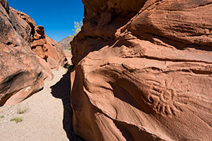 Where is This? photograph of a sun symbol etched into a red sandstone wall along a sandy path is by Elias Butler