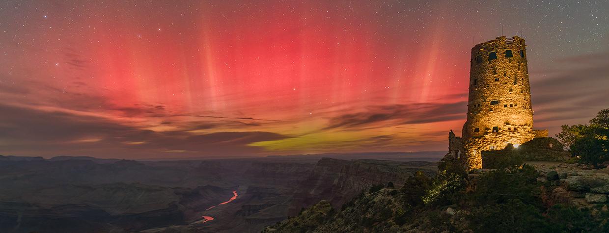 The aurora borealis fills the night sky over the Grand Canyon in a view from Desert View Watchtower, on the East Rim, in October 2024. Far below the rim, the Colorado River mirrors the red hues of the northern lights. | Rich Rudow