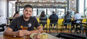Armando Hernandez with food and drink at a table in Cocina Chiwas with the bar in the background. By Paul Markow