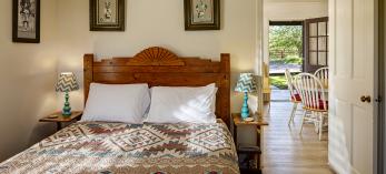 Interior of cottage bedroom shows view through front room through open door to outside. By Steven Meckler